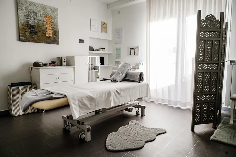 Sala luminosa dello studio con lettino elettrico da massaggio e paravento in legno