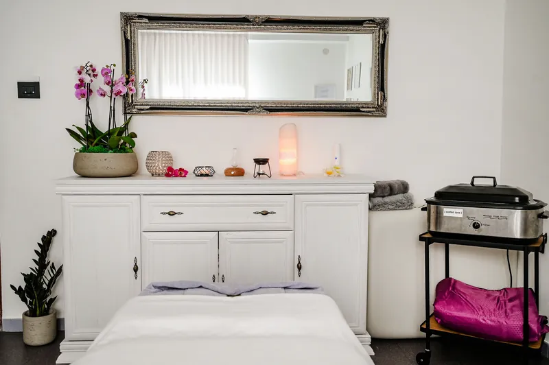 Massageraum: weiße Kommode mit Orchidee, Salzlampe und Spiegel über der Massageliege