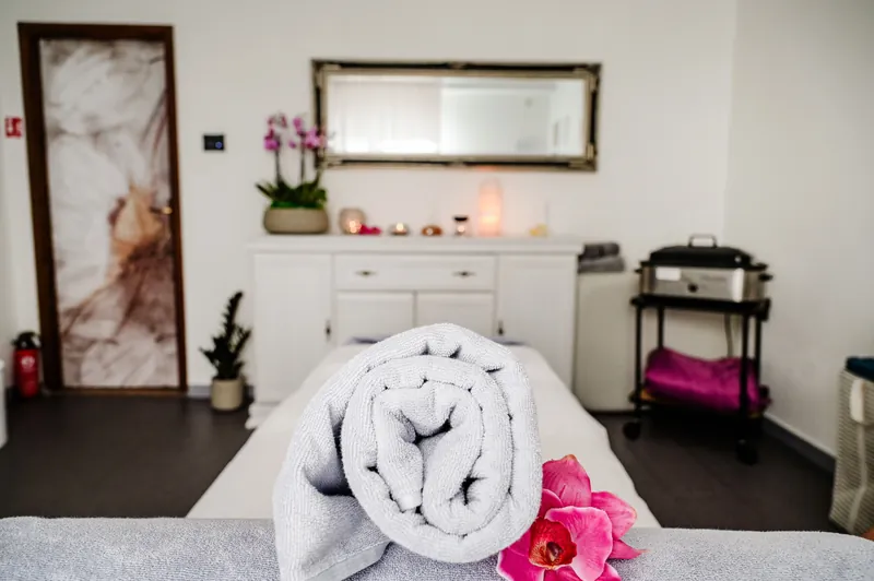 Massageraum im Studio Physio Art Lara: gerolltes Handtuch mit Orchidee auf der Massageliege, Spiegel und Kerzen im Hintergrund