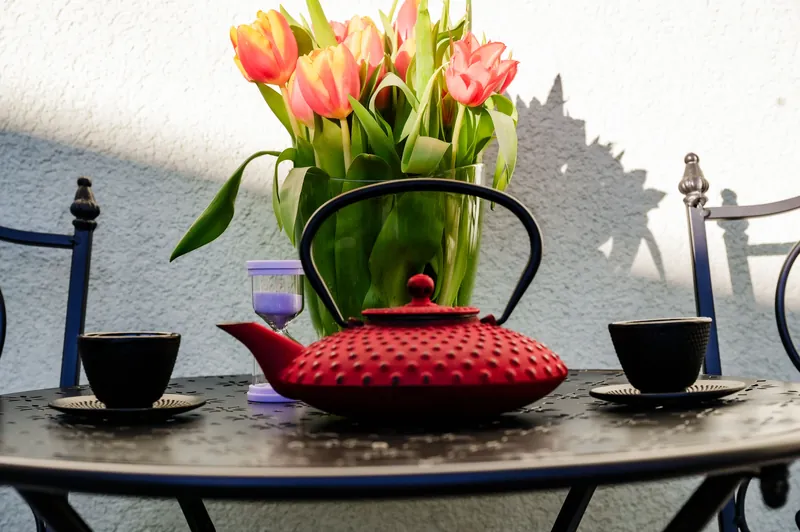 Rote Teekanne, Tassen und Tulpen auf einem Tischchen auf der Terrasse des Studios