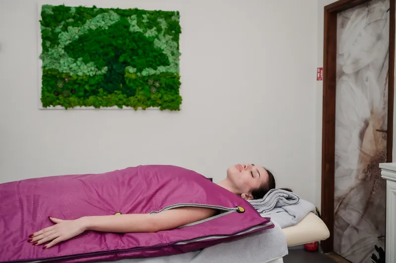 Impacco corpo nella coperta termica viola, parete verde di muschio sullo sfondo